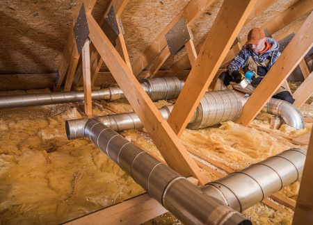 A worker is fixing the ventilation ducts in an attic filled with insulation material. The setting is a residential home during the cold winter months.