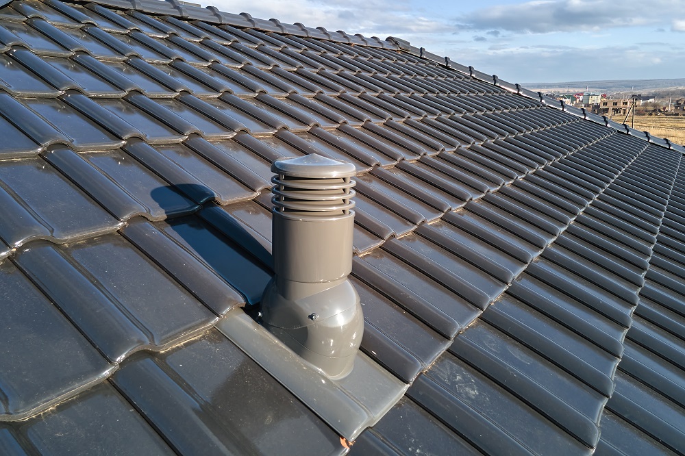 Closeup of ventilation pipe on house roof top covered with ceramic shingles. Tiled covering of building.