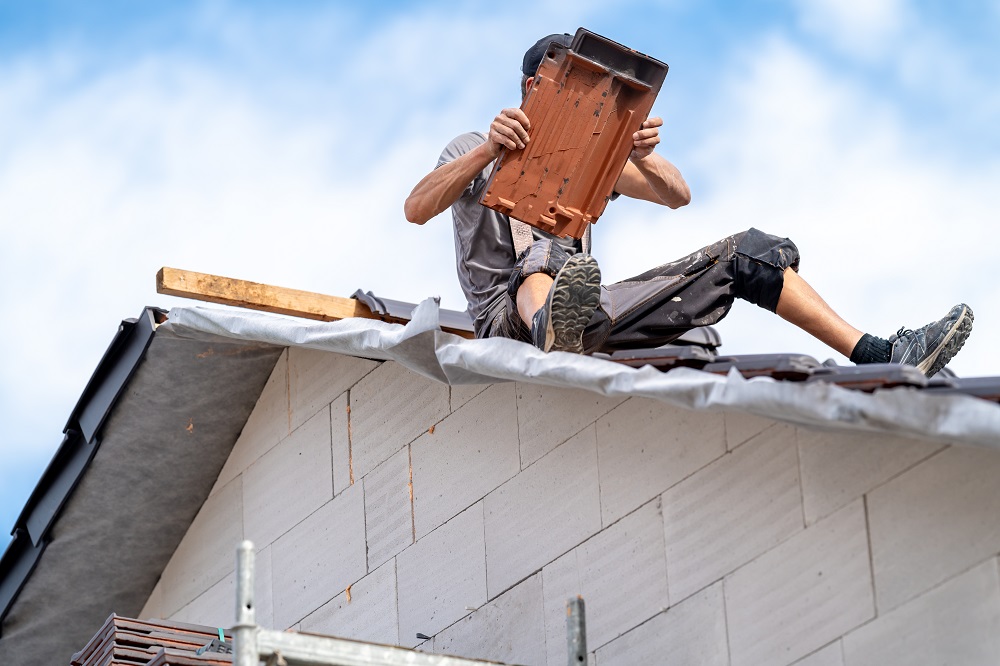 roofer with ceramic tile in hand on roof of house.